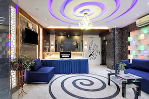 Un vestíbulo de hotel con una recepción, sofás azules, una araña y un piso de mármol.