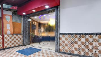 Un vestíbulo de hotel con una mesa de recepción, un felpudo azul, baldosas de suelo con diseños y un techo rojo.