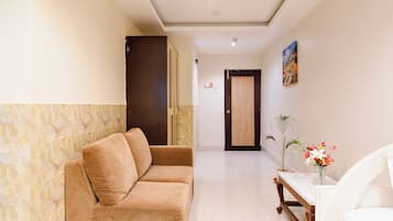Um hall de hotel com um sofá, uma mesa com um vaso de flores, um quadro na parede e uma porta.