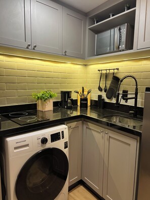 A compact kitchen with a built-in washing machine, a coffee maker, and utensils hanging on the wall. - New Listing (Rio de Janeiro)