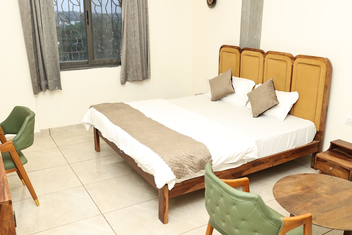 A bedroom with a bed, a green chair, a wooden nightstand, and a round wooden table.