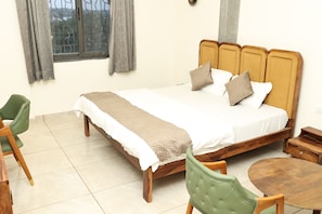 A neatly arranged hotel room with a bed, a chair, a small table, and a window with curtains. - Indraprastha Resort (Barmer Gadan)
