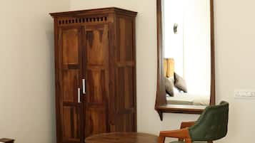 A bedroom with a bed, a wooden wardrobe, a chair, a round table, and a wall-mounted air conditioning unit.
