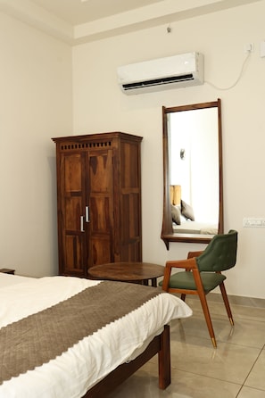 A bedroom with a bed, a wooden wardrobe, a chair, a round table, and a wall-mounted air conditioning unit. - Indraprastha Resort (Barmer Gadan)