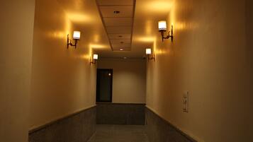 A corridor with wall-mounted sconces, a ceiling light, and a door at the end.