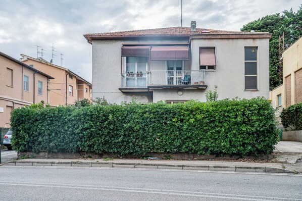 A two-story residential building with a balcony, a window with shutters, and a hedge in front. - Casa Valeria (Ancona)