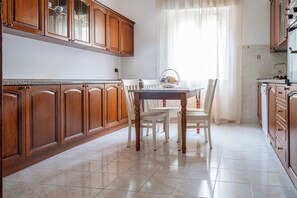 A kitchen with wooden cabinets, a dining table with chairs, and a window with sheer curtains. - Casa Valeria (Ancona)