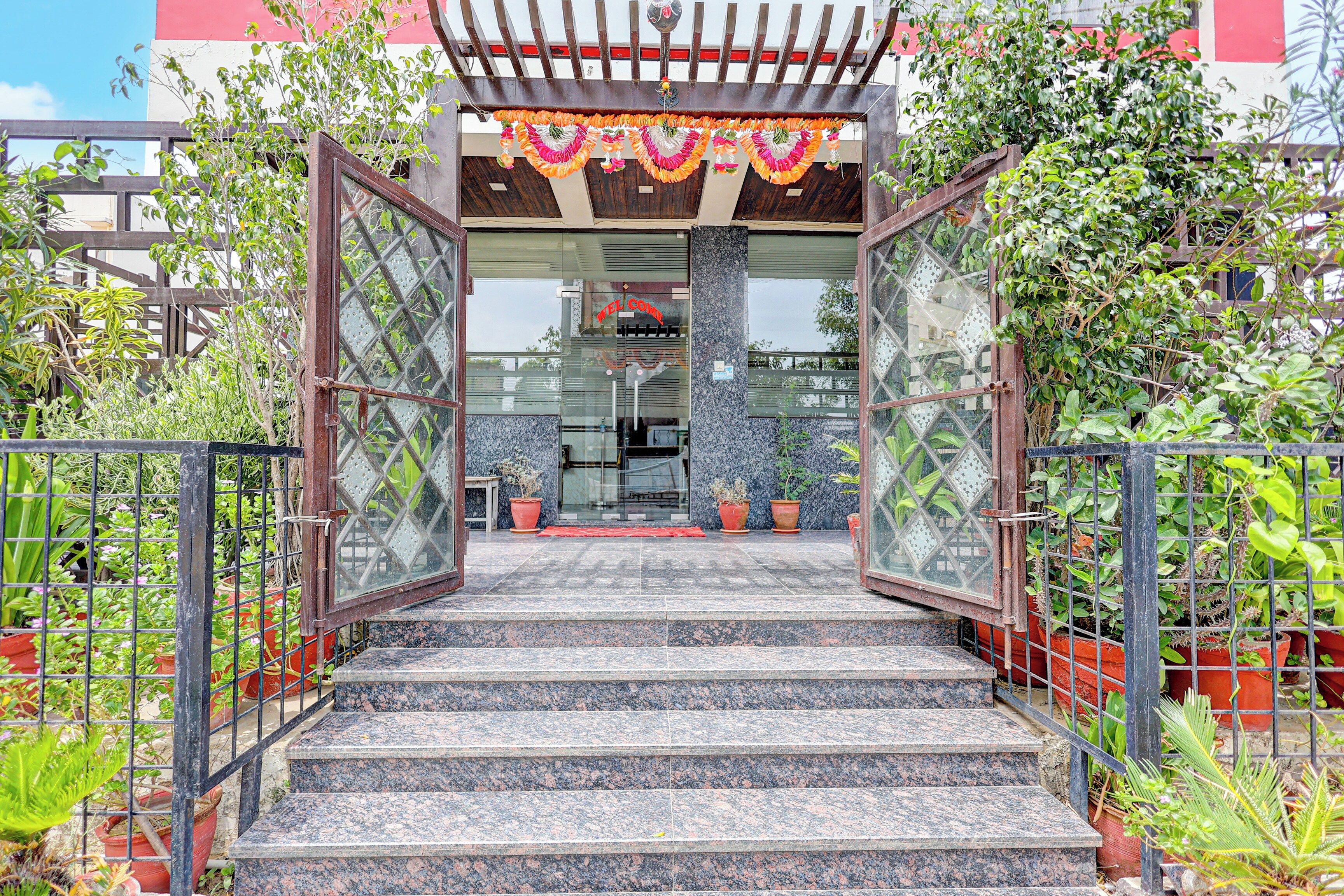 Una escalera conduce a la entrada de un edificio, con una puerta de cristal, rodeada de macetas y una valla de metal.