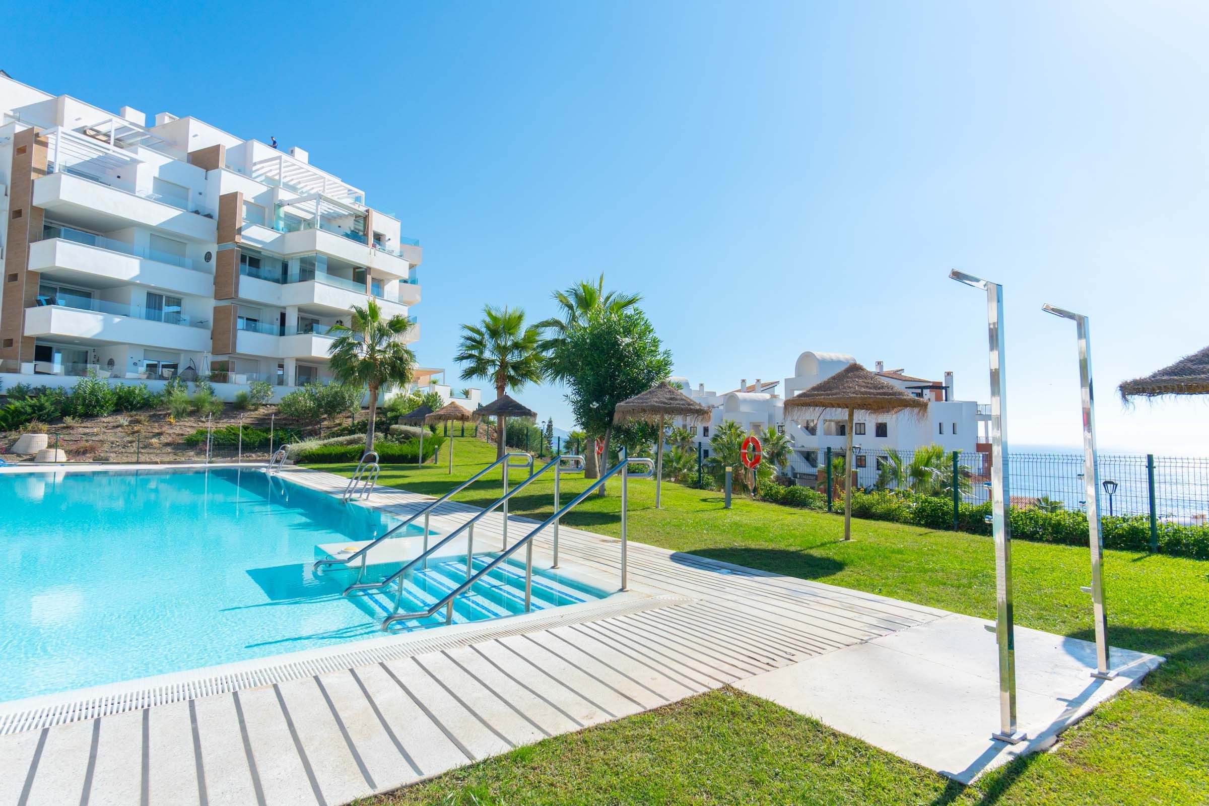 Un hotel modern amb piscina, zona de seients a l'exterior i vista al mar.