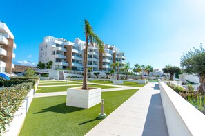 Un complesso residenziale moderno con un cortile centrale, una palma e un cielo azzurro.