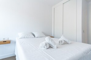 A minimalist hotel room with a bed, pillows, a wooden nightstand, and a wall-mounted power outlet. - Luxury Seaview Isea 2231 by Casasol (Torrox)