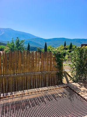 A wooden fence with a metal mesh in the foreground, a clear blue sky, and a mountainous landscape in the background. - Lodge des Baronnies II - Les Cabanes de Provence (Plaisians)
