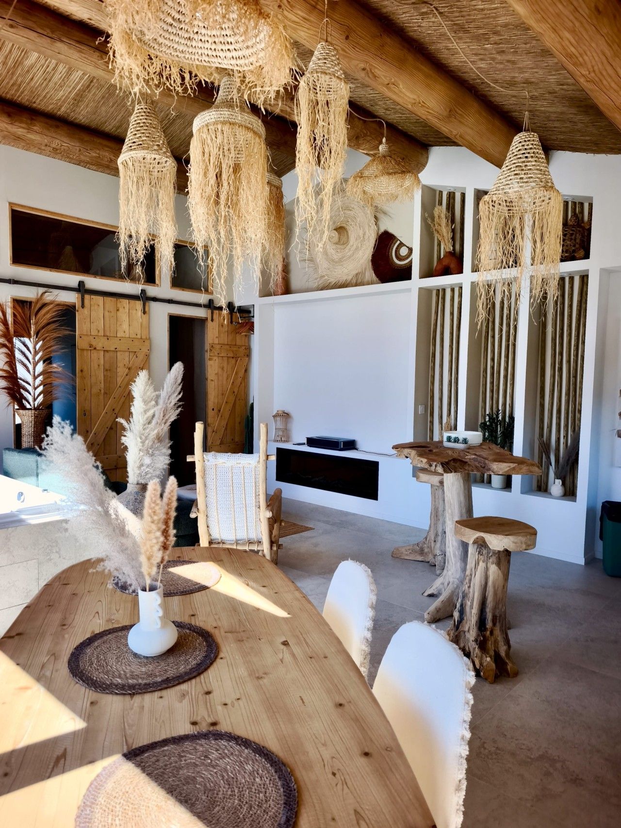 Un interior moderno con una mesa de comedor de madera, lámparas de macramé colgantes y un banco rústico de madera.