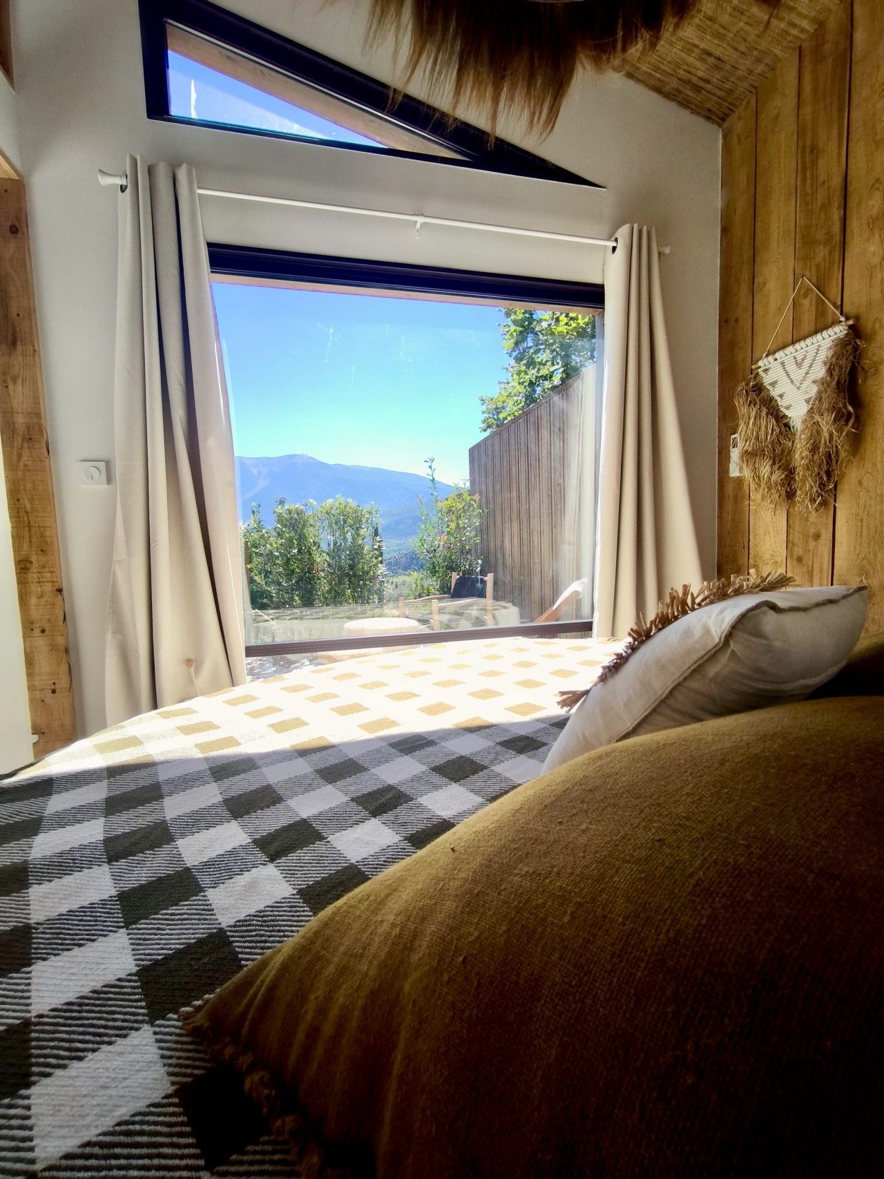 Un dormitorio con un ventanal grande, una colcha a cuadros y vistas al exterior.