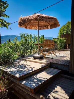 A wooden deck with a thatched umbrella, outdoor seating, and a view of mountains.