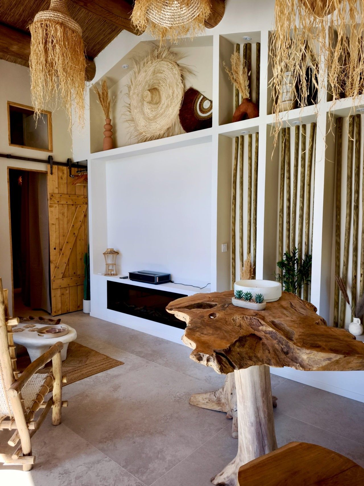 Een landelijk interieur met een houten eettafel, een open haard en een hangende geweven lamp.