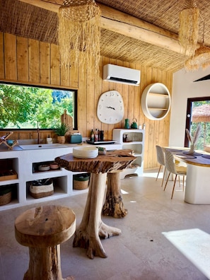 A modern interior with a wooden ceiling, a large window, a round wall clock, and a dining area with a white table and chairs.