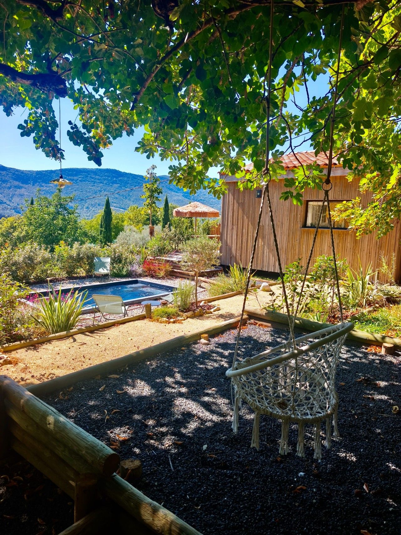 Un patio trasero con terraza de madera, un columpio colgante, una piscina pequeña y vistas a montañas.