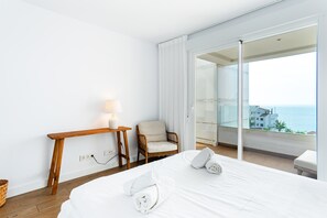 Et hotelværelse med en seng, en stol, et lille bord med en lampe og havudsigt fra en balkon.