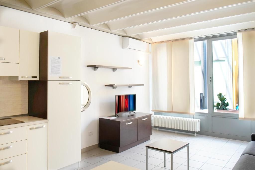 Een moderne keuken met witte kastjes, een donker aanrecht en een kleine tafel. Er is een raam met gordijnen en een radiator eronder.