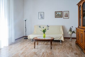 Ein Zimmer mit einer Couch, einem runden Holztisch mit Blumen in einer Vase und einem Schrank.