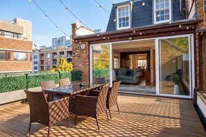 An outdoor deck with a glass door leading to a living area, wicker furniture, and a view of the cityscape. - Family Home near Angel with Terrace - Pass the Keys (London)