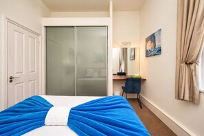 Habitación de hotel con cama, escritorio, silla, armario y ventana con cortinas.
