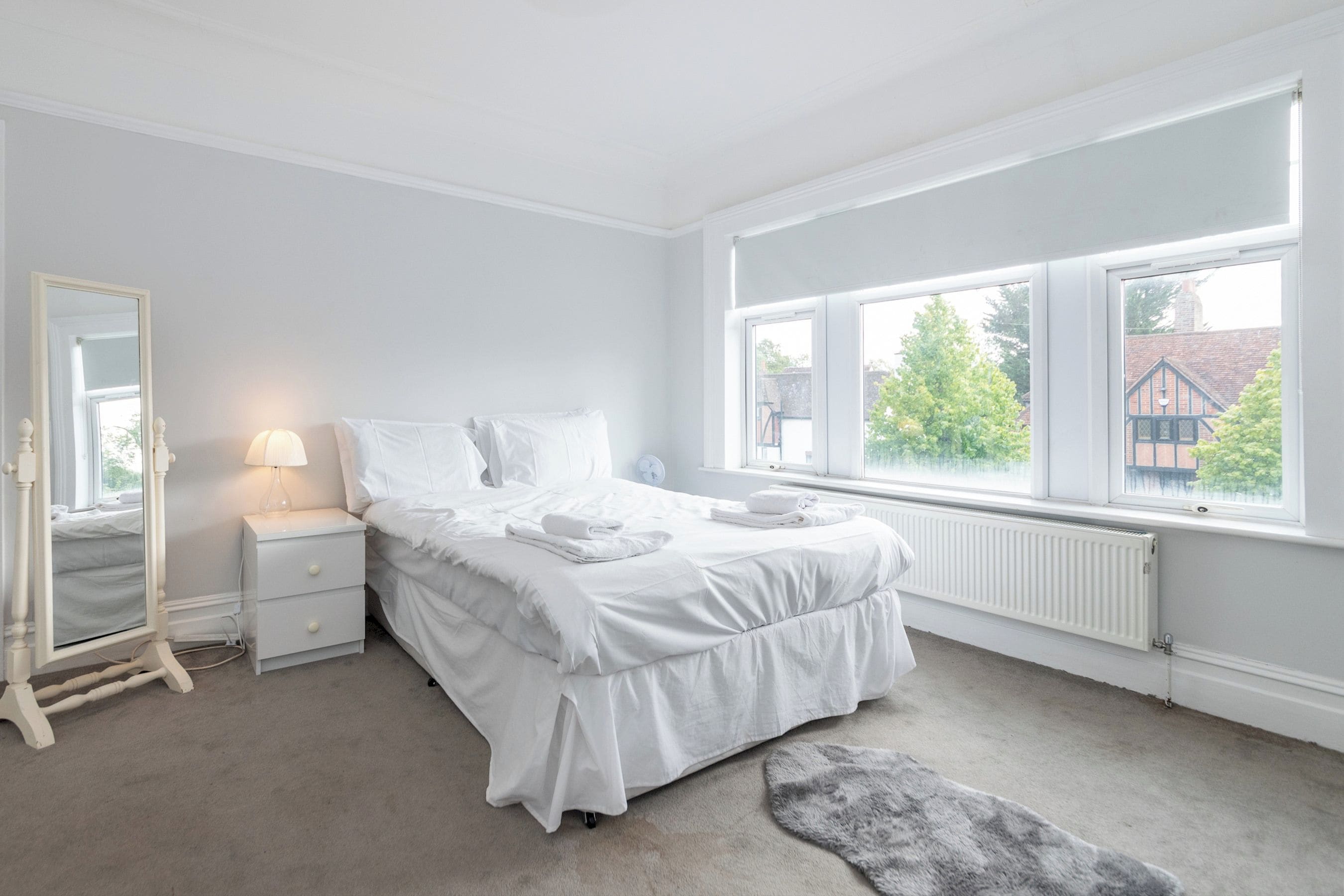 Une chambre à coucher avec un lit, une table de chevet, un miroir et une fenêtre donnant sur l’extérieur.