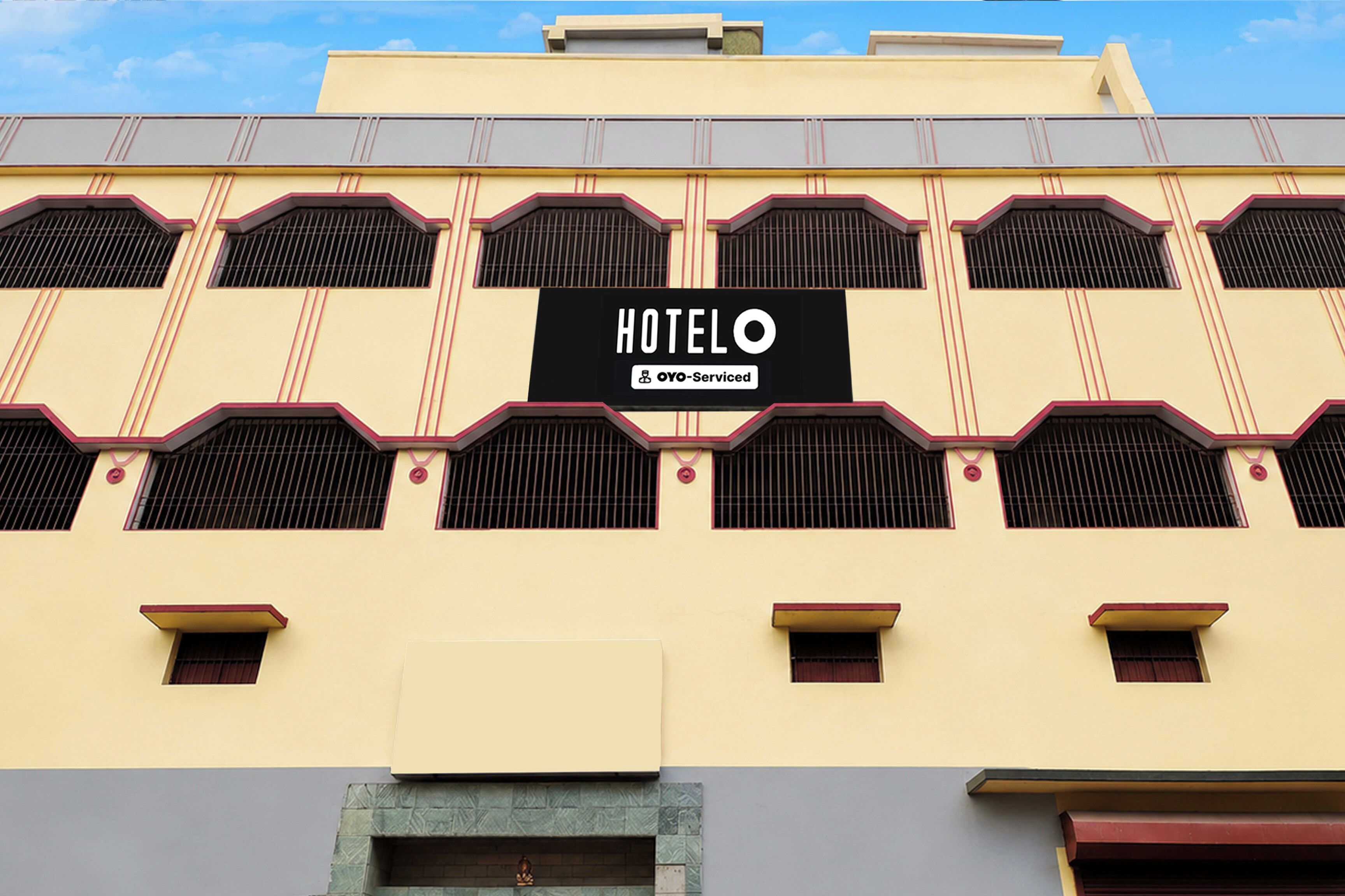 Un hôtel avec une enseigne indiquant « HÔTEL O YO-Serviced », et un style architectural distinctif caractérisé par de nombreuses fenêtres et un toit plat.