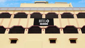 Un hôtel avec une enseigne indiquant « HÔTEL O YO-Serviced », et un style architectural distinctif caractérisé par de nombreuses fenêtres et un toit plat.