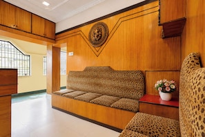 A reception area with a wooden reception desk, a sofa with a leopard print cushion, and a decorative emblem on the wall. - Super Hotel O Badambadi Bus Terminal (Cuttack)