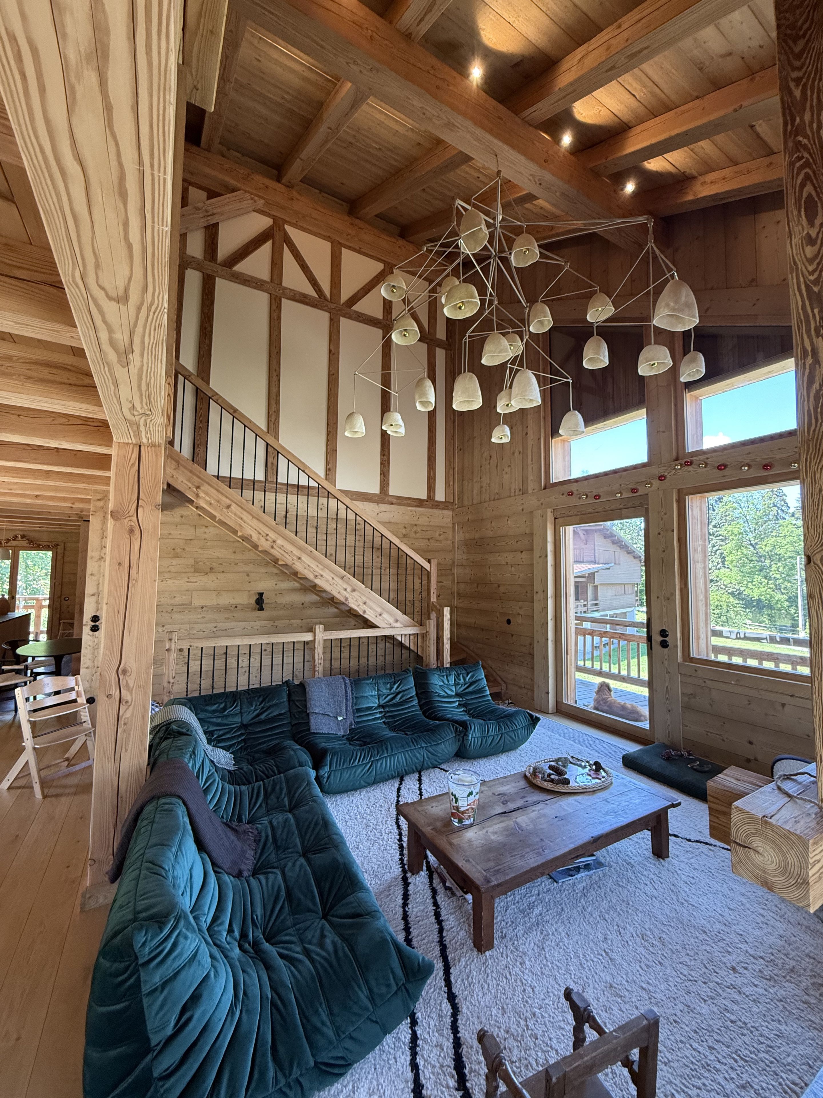 Une pièce spacieuse avec un grand canapé d’angle, un escalier en bois et un luminaire au plafond au design original.