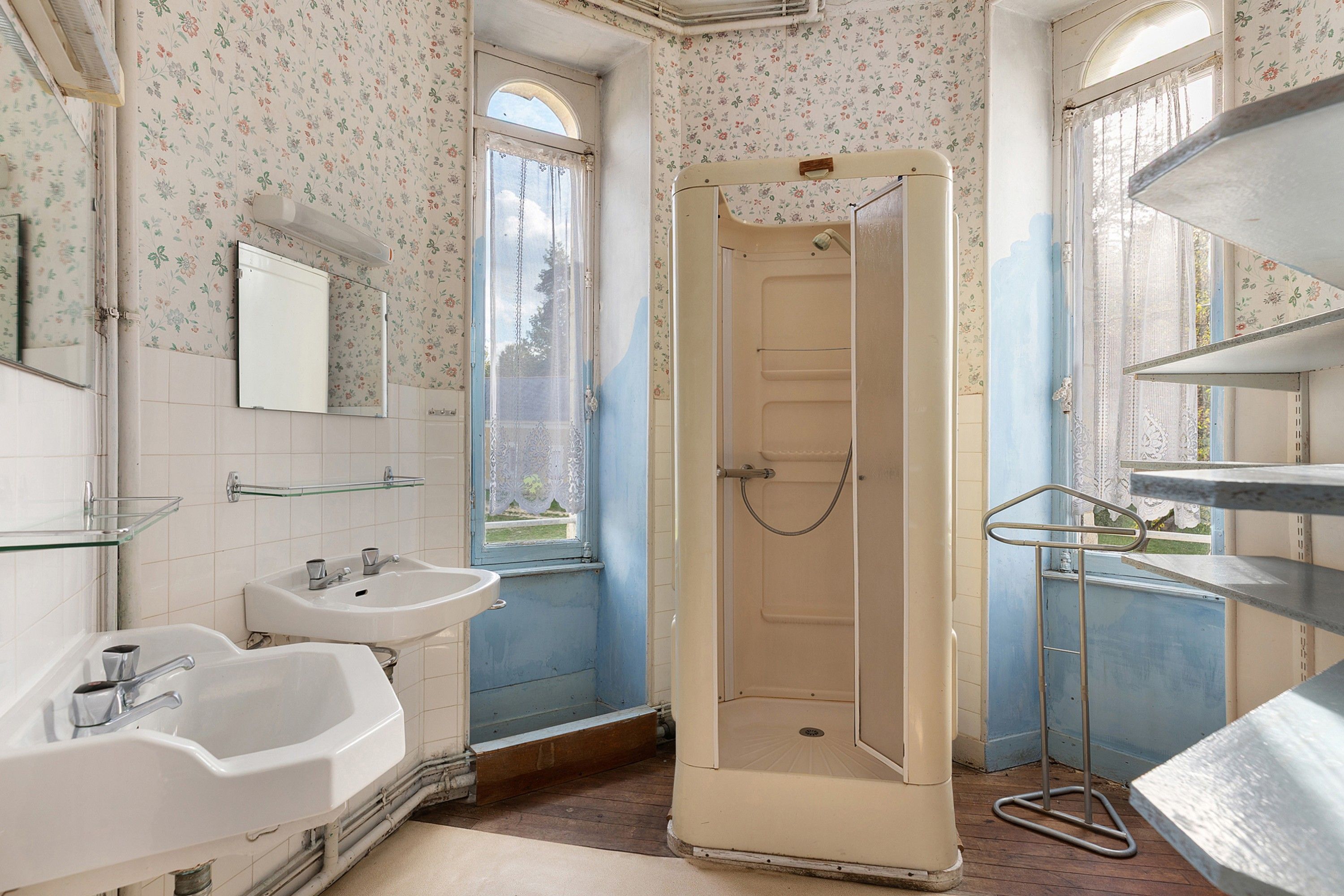 Une salle de bain avec deux lavabos, une douche et une fenêtre ornée d’un papier peint à motifs floraux.