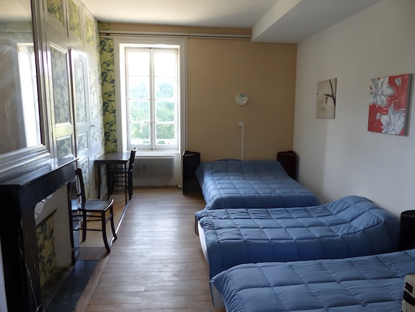A room with two beds, a chair, a radiator, a window, and artwork on the walls.
