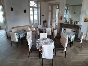 A dining area with multiple tables and chairs, a fireplace, and a view through the glass doors. - Château de Grésillon - Sleeps 60 - 18-hectare grounds (Baugé-en-Anjou)