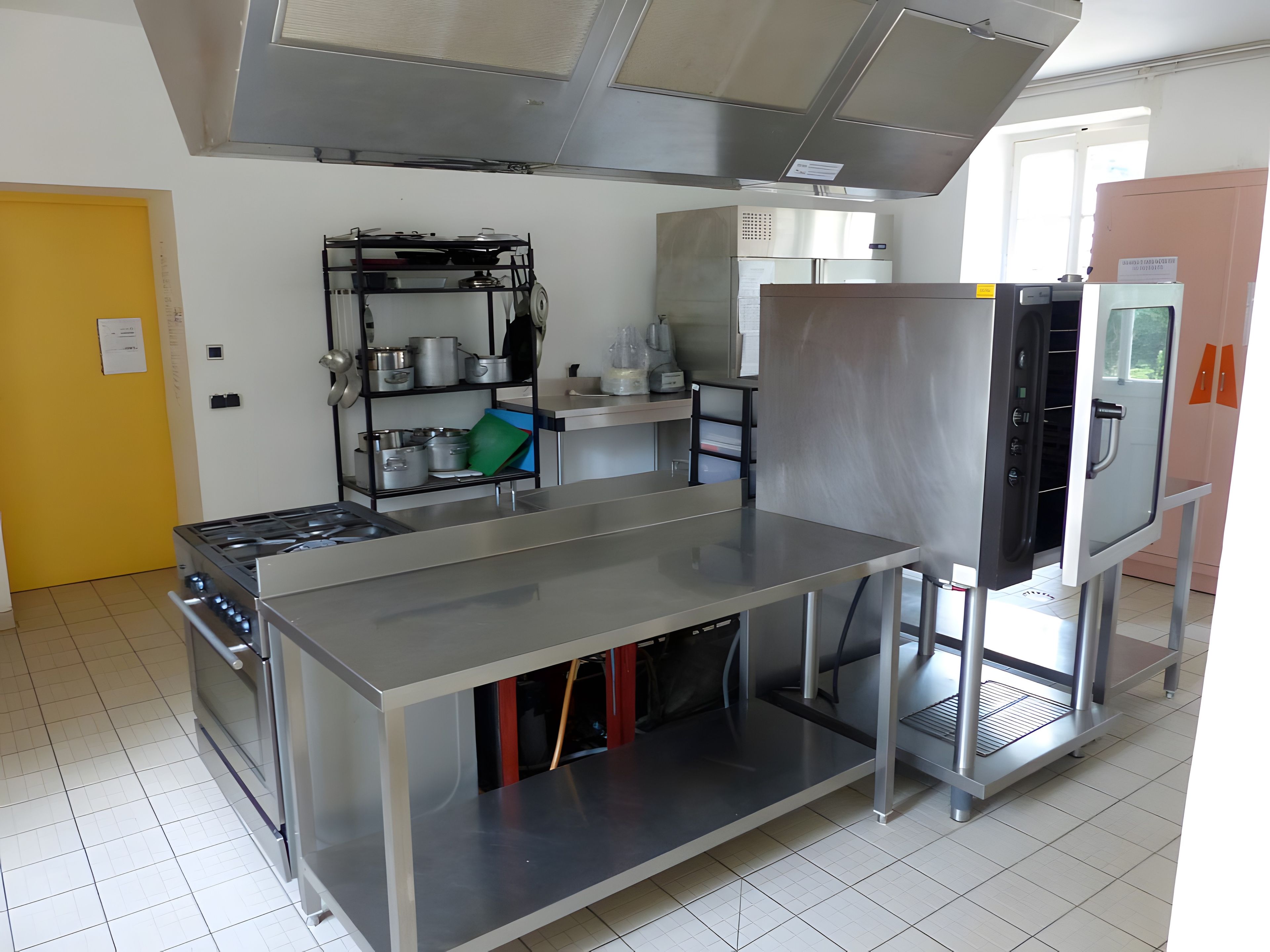 Une cuisine professionnelle équipée d’appareils en acier inoxydable, d’un grand plan de travail et d’un réfrigérateur.