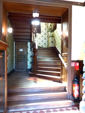 A wooden staircase leading to a door with a fire extinguisher on the right.
