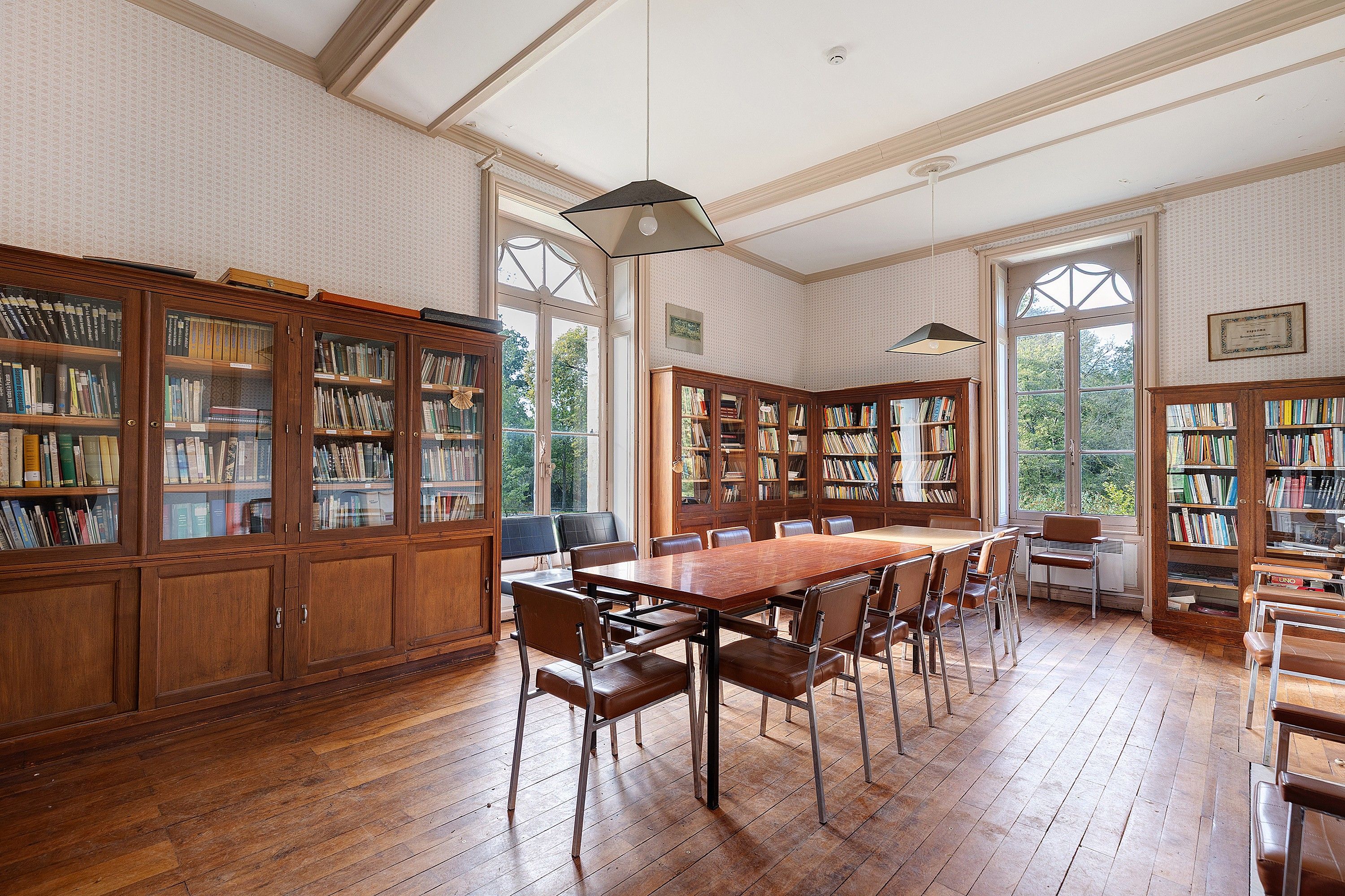 Une bibliothèque avec des étagères en bois, une grande table en bois et des fauteuils en cuir.