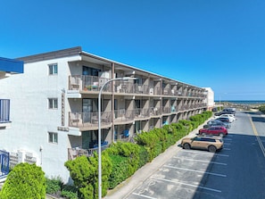 A multi-story hotel with balconies, a parking lot, and a clear view of the ocean. - Oceanside 1BR Condo Close to Beach (Ocean City)
