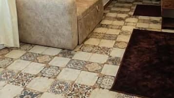 Sala de estar com ladrilhos estampados, um sofá, um tapete escuro e um espelho na parede.