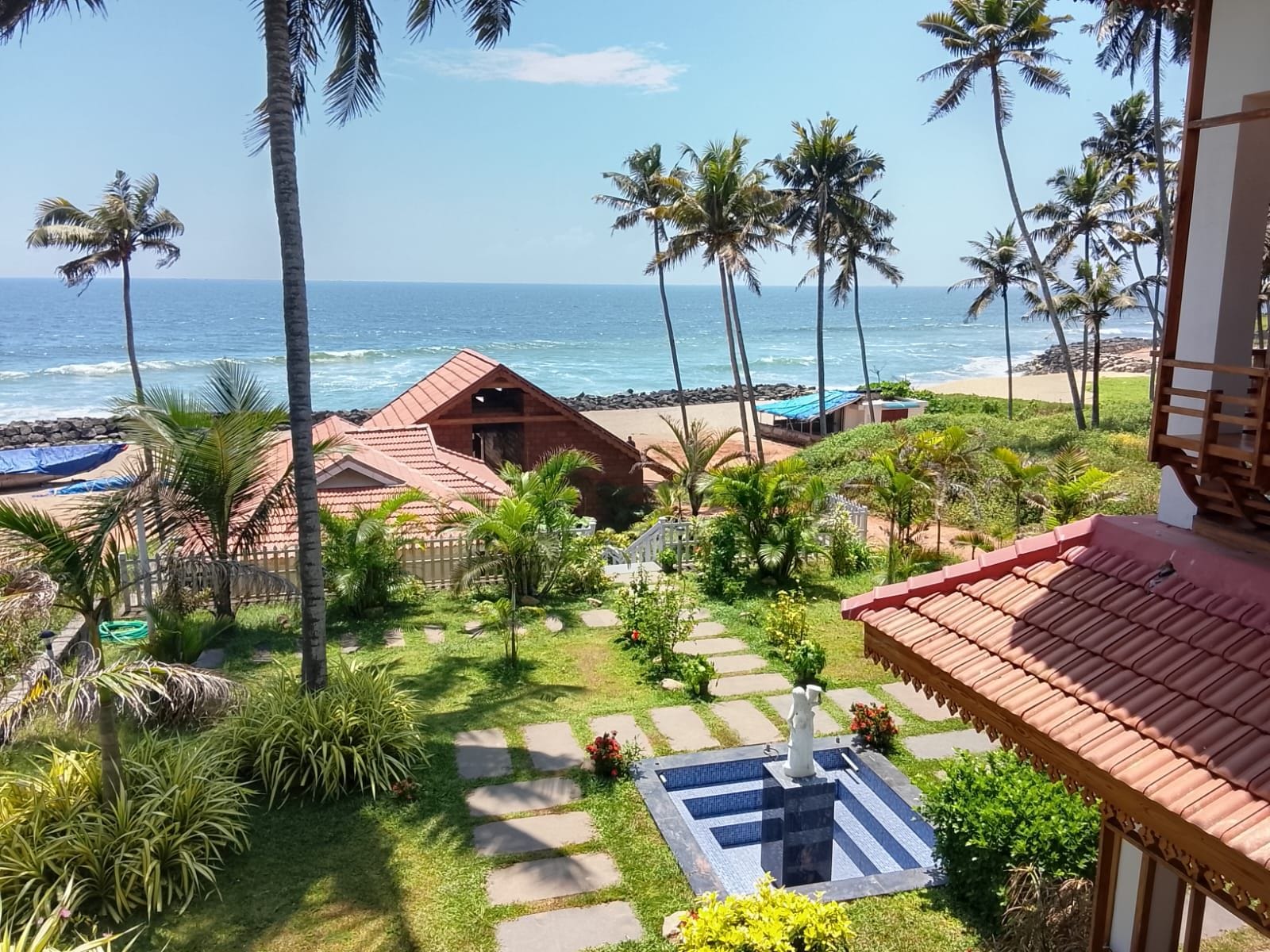 A beachfront property with a swimming pool, palm trees, and a view of the ocean.