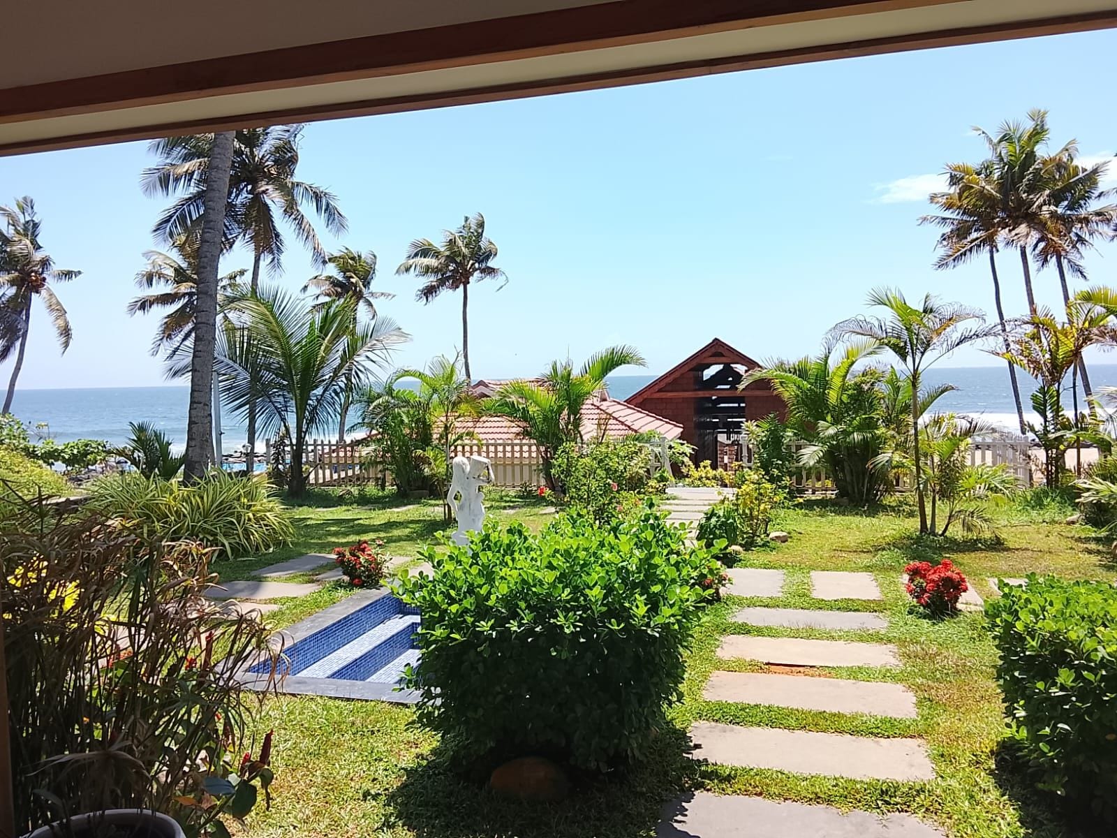 A resort with a paved pathway leading to a building, surrounded by palm trees and a view of the ocean.