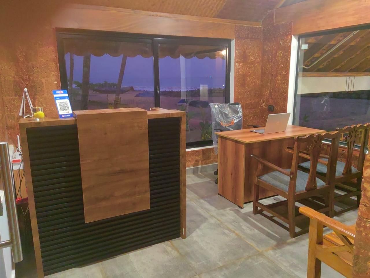 Un comptoir d’accueil avec un ordinateur portable, des chaises en bois et une vue sur la plage au crépuscule.