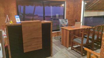 Un comptoir d’accueil avec un ordinateur portable, des chaises en bois et une vue sur la plage au crépuscule.