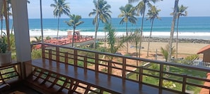 Un balcón con vista a una playa, palmeras y el océano.