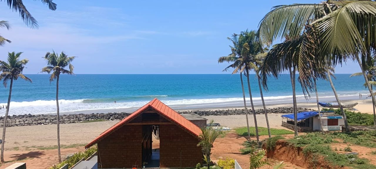 A beach view with a small brick building, palm trees, and a clear blue ocean.