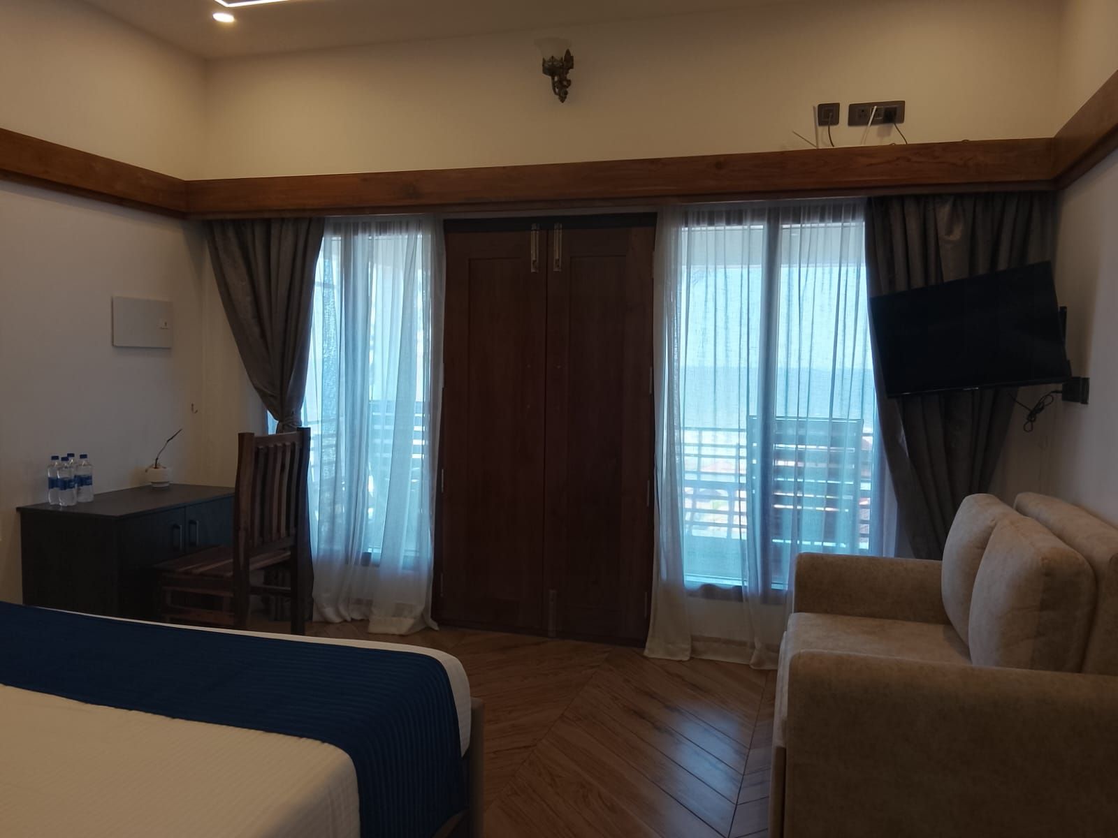Une chambre d’hôtel équipée d’un lit, d’un bureau, d’une chaise, d’un canapé et d’un téléviseur fixé au mur.