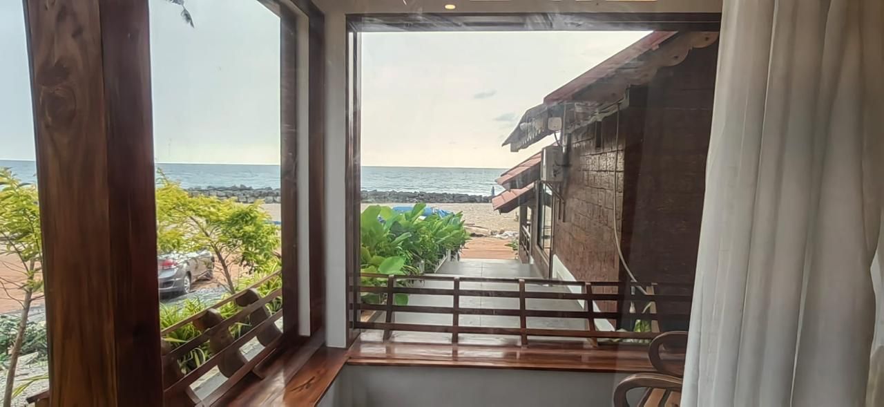 Ein Zimmer mit Blick auf den Strand, Holzboden, ein Fenster mit Ausblick und ein Balkon mit Geländer.