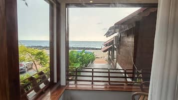 Una habitación con vistas a la playa, suelo de madera, un ventanal y un balcón con barandilla.