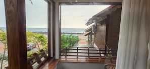 A room with a view of the beach, wooden flooring, a window with a view, and a balcony with a railing. - Flower Hill Cottage (Varkala)
